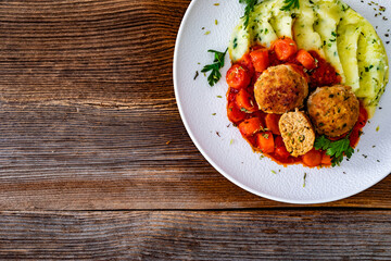 Fried pork meatballs and carrots in tomato sauce with mashed potatoes on wooden table