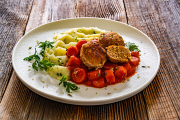 Fried pork meatballs and carrots in tomato sauce with mashed potatoes on wooden table