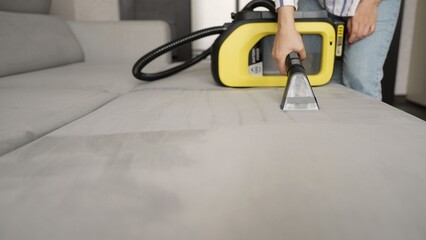 Housekeeper cleaning gray sofa with vacuum cleaner
