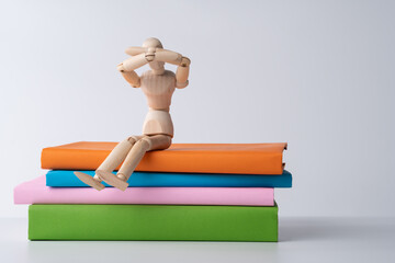 Wooden Figurine on Books: A wooden figurine sits on a stack of colorful books, symbolizing education, knowledge, and the pursuit of learning.