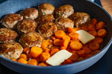 Frying pork meatballs and carrots in frying pan on electric stove