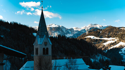 Historic alpine church tower rising above forested valley with rugged peaks beyond, South Tyrol...