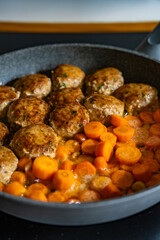 Frying pork meatballs and carrots in frying pan on electric stove