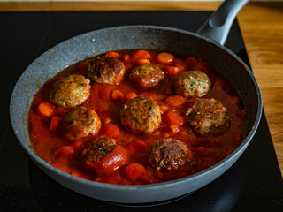 Cooking fried pork meatballs and carrots in tomato sauce in frying pan on electric stove