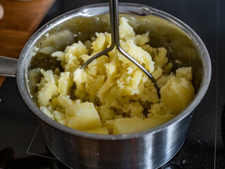 Mashing potatoes in pot on electric stove, close-up