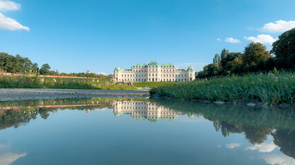 Fototapeta premium Serene palace reflection in calm lake under blue sky in Vienna Austria ideal for travel and nature photography