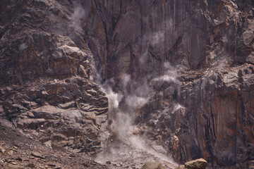 A rock fall in the mountains. A pillar of dust from a falling rock on a cliff