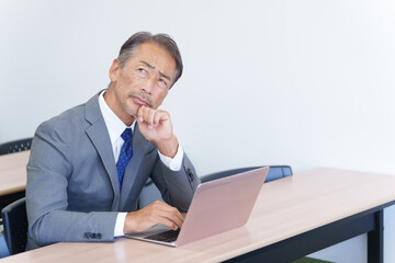 パソコンを見て考えるシニアビジネスマン