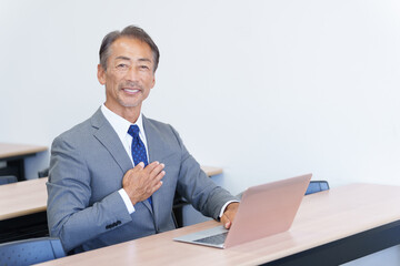 パソコンを使い胸に手を当てるシニアビジネスマン