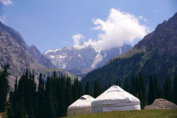 White nomadic yurts in a mountain valley overlooking snow-covered peaks and forests. Traditional...