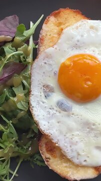 Croque Madame or Grilled cheese with ham and egg on a wooden cutting board. The sandwich is toasted and has a runny yolk and salad in restaurant