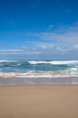 Ocean Waves Crashing on Sandy Beach under Blue Sky