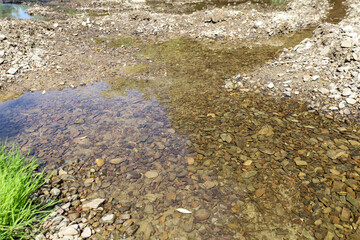 Fragile streams of clear water flow over a shallow bottom covered with colorful stones and small...