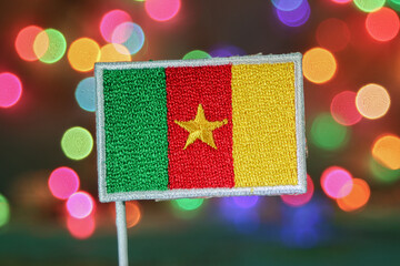 Cameroon flag embroidery with vibrant rainbow bokeh lights resembling fireworks. Perfect for New Year or holiday celebration themes with festive city atmosphere.
