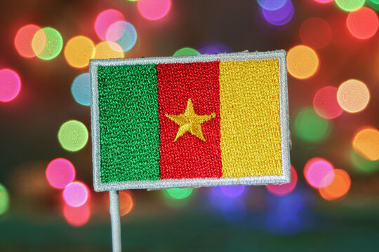 Cameroon flag embroidery with vibrant rainbow bokeh lights resembling fireworks. Perfect for New Year or holiday celebration themes with festive city atmosphere.