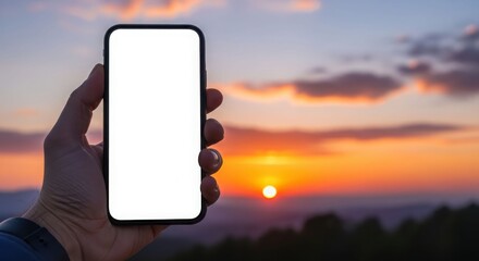 A hand holding a smartphone with a blank screen against a vibrant sunset.