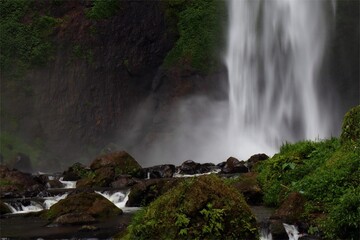 Pelangi Waterfall, West Bandung, Indonesia, surrounded by lush green foliage, vibrant nature, rainbow mist, cascading water, serene, tropical scenery, eco-tourism, hiking.