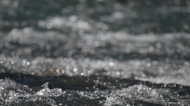 Close-up view of a small river with rushing churning water reflecting the sun creating highlights
