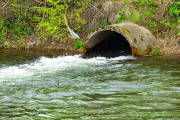 Water flows from a drainage pipe into a natural river surrounded by greenery and vegetation on a...
