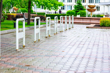 Pathway lined with bike racks in a green park setting, featuring benches and a fountain surrounded...
