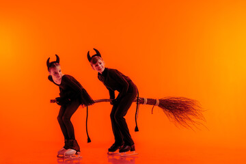 Young figure skaters perform on ice dressed as devils for Halloween against a bright orange background