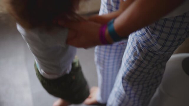 Toddler crying for attention and pushing mother away from kitchen counter before she finally lifts him into her arms, candid emotional family moment at home