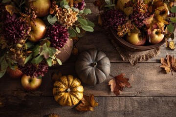A rustic autumnal display of pumpkins, apples, flowers, and leaves on a weathered wooden surface, evoking a sense of harvest and tranquility.
