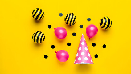 Festive party arrangement with balloons, a polka dot hat, and confetti on a bright yellow background, perfect for a birthday celebration