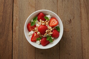 Freshly prepared cottage cheese served with strawberries, mint leaves, and nuts on a rustic wooden surface. Healthy morning meal. Nutritious eating.