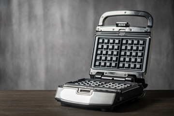 Modern open waffle iron on wooden table, closeup. Electric waffle maker in the home kitchen