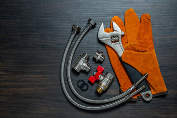 Adjustable wrench, ball valve with red handle, stainless steel tee fittings, leather safety gloves and rubber gaskets on wooden background, top view, copy space, closeup. Plumbing repair concept