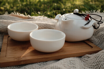 White China style teapot with lid and two empty cups on a wooden tray, placed outdoors on a blanket