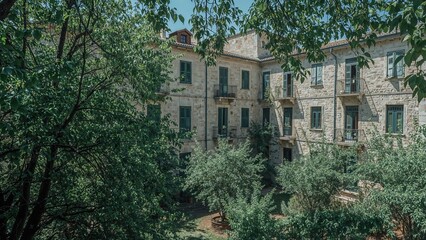 Vintage stone-built quarter with balconies immersed in a leafy courtyard abundant with trees and bushes, providing a shaded, comfortable atmosphere in the summer