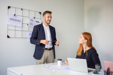 Businessman discussing project with female colleague during office meeting, teamwork collaboration with laptop and sales report charts, corporate communication concept.