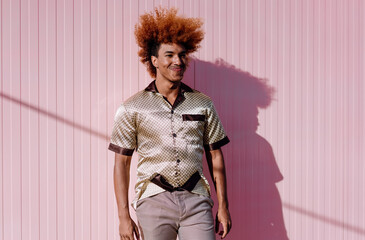 Young African American man with curly ginger hair smiling brightly in sunlight, posing casually...