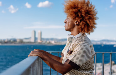 Relaxed man with curly red afro, headphones resting on neck, smiling with eyes closed, representing digital freedom, leisure, and immersive personal audio technology outdoors.