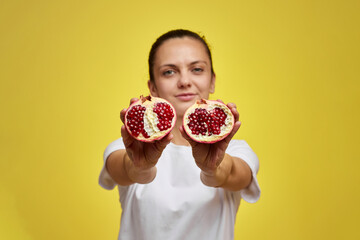 Beautiful happy woman holding pomegranate on yellow background, focus on pomegranate