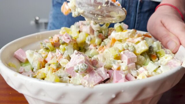 Close up video of woman mixing traditional Olivier salad in bowl. Homemade festive dish with vegetables, sausage, potatoes, eggs, mayonnaise. Popular Russian cuisine recipe for holiday