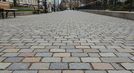 Walkway cobblestones leading to city buildings with benches and lamps, inviting urban exploration