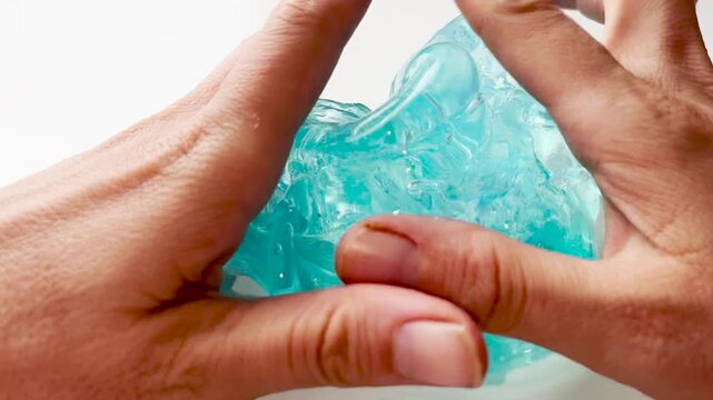 A woman or teenage girl relieves stress by playing with blue slime, stretching and squeezing it on a white table for relaxation, fun, and sensory activity.