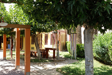Stock photo of a sunny courtyard with a wooden pergola, picnic tables, and colorful hanging...