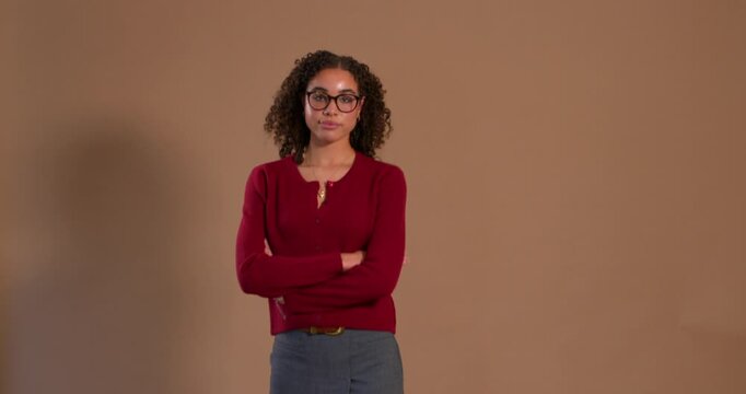 Video clip of a young adult female in the studio, smiling while walking into frame and then towards the camera, folding her arms with a cool attitude. She has brunette curly hair 