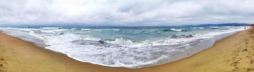 Scenic beach panorama capturing ocean waves under a cloudy sky