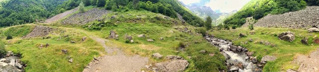 Panoramic view of a lush green valley with a stream and rocks