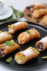 Delicious cannoli with cheese, nuts, powdered sugar, chocolate and mint on table, closeup