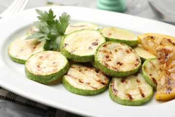 Delicious fried courgette slices with lemon and parsley on table, closeup