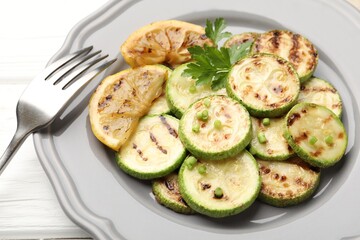 Delicious fried courgette slices with lemon, green onion and parsley on white wooden table, closeup