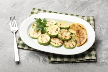 Delicious fried courgette slices with lemon and parsley served on grey table, closeup