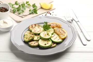 Delicious fried courgette slices with lemon and parsley served on white wooden table, closeup