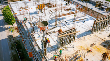 Aerial view on masons fill up vertical mold with help of crane as carry cone tank for cement mixture